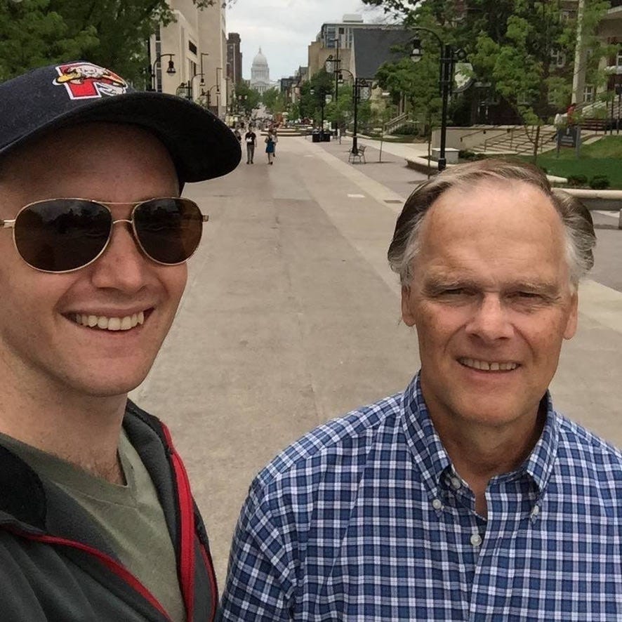 A selfie of Ned Donovan and W Michael Donovan smiling on the street of in Madison Wisconsin in 2015. In the background is the Wisconsin Capital building.