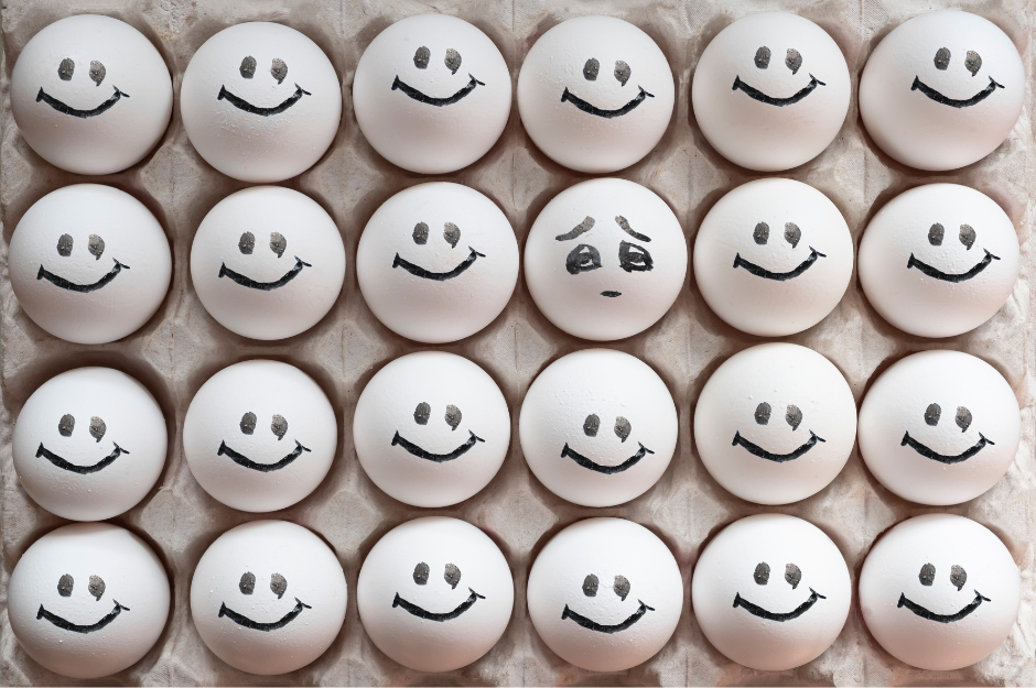 A row of eggs with smiling faces, and one egg with a frowning face. 