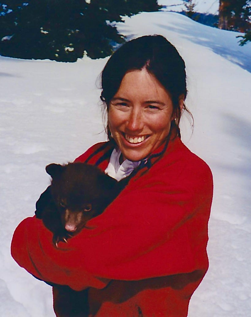 Photo of Kris as a younger woman in a red jacket, holding a small bear cub.