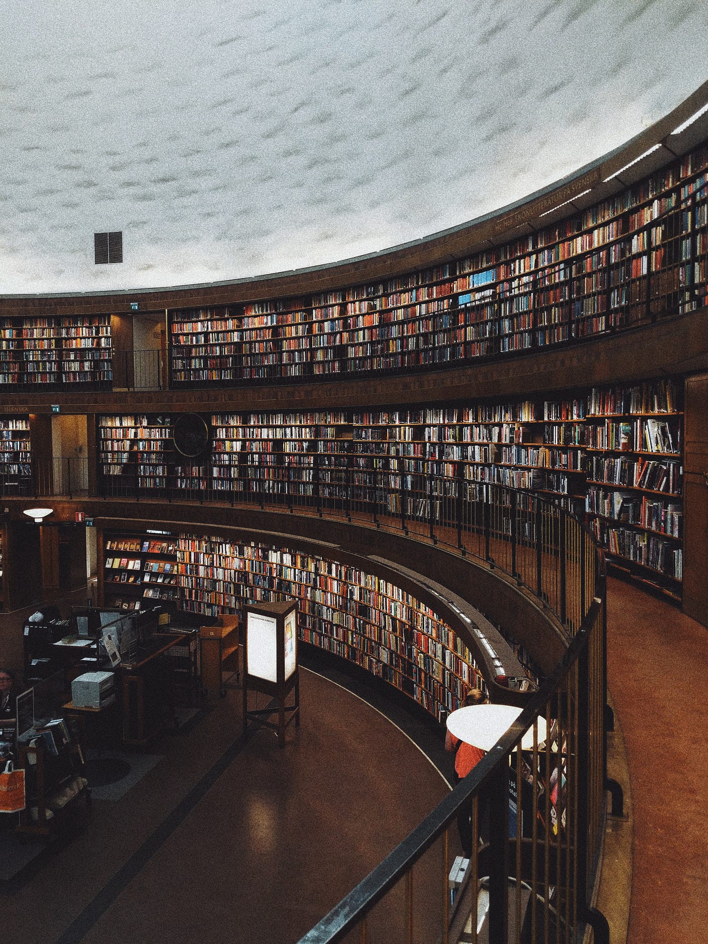 A curve shaped library with brown accents and thousands of books