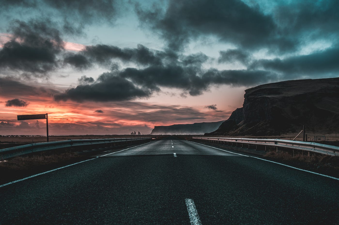 A long open highway with the sun rising and the sky turning crimson.
