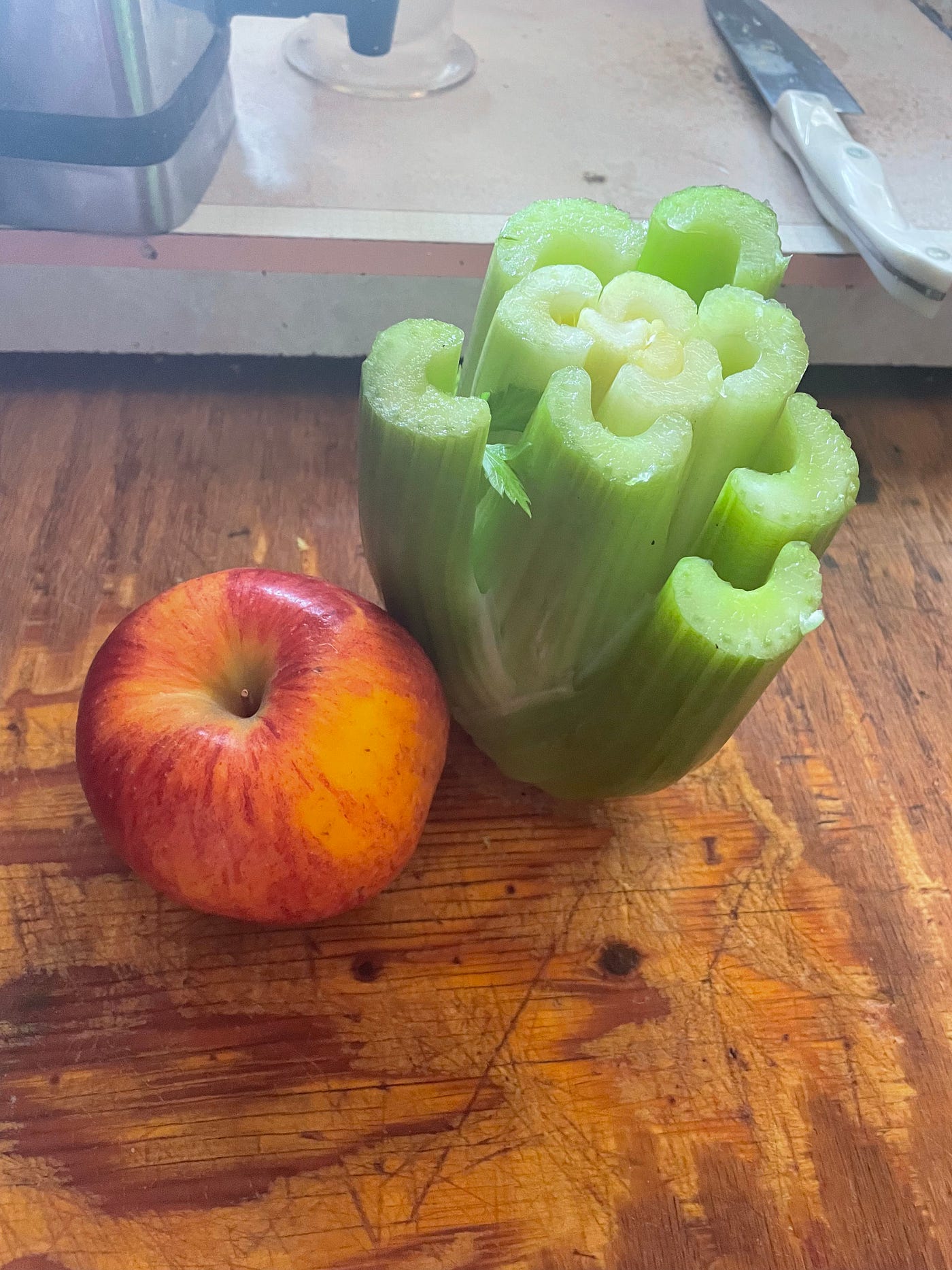 An apple and half a stock of celery on a cutting bord.