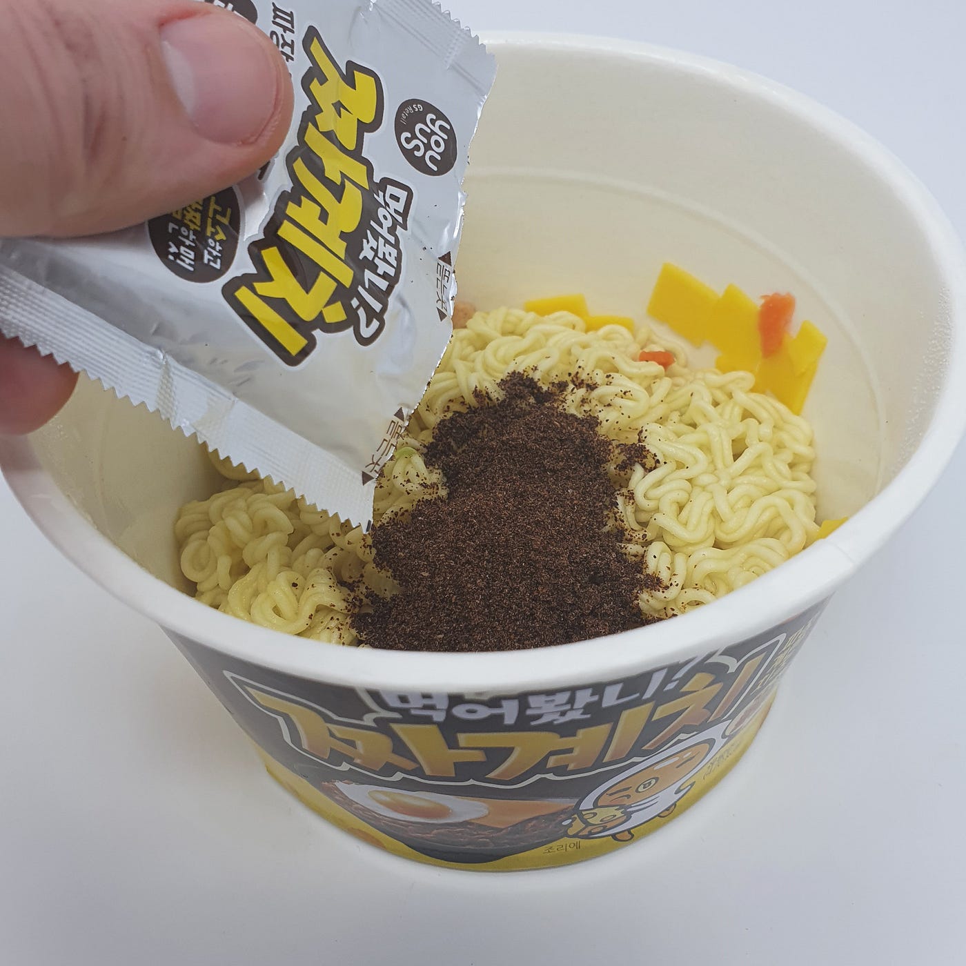 Adding the powdered jjajang packet to a cup of YouUs Jjagyechi Instant Noodles.