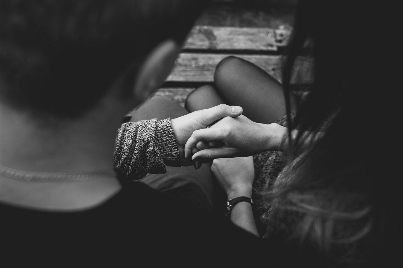 A black and white photo of a girl and guy sitting together holding hands.