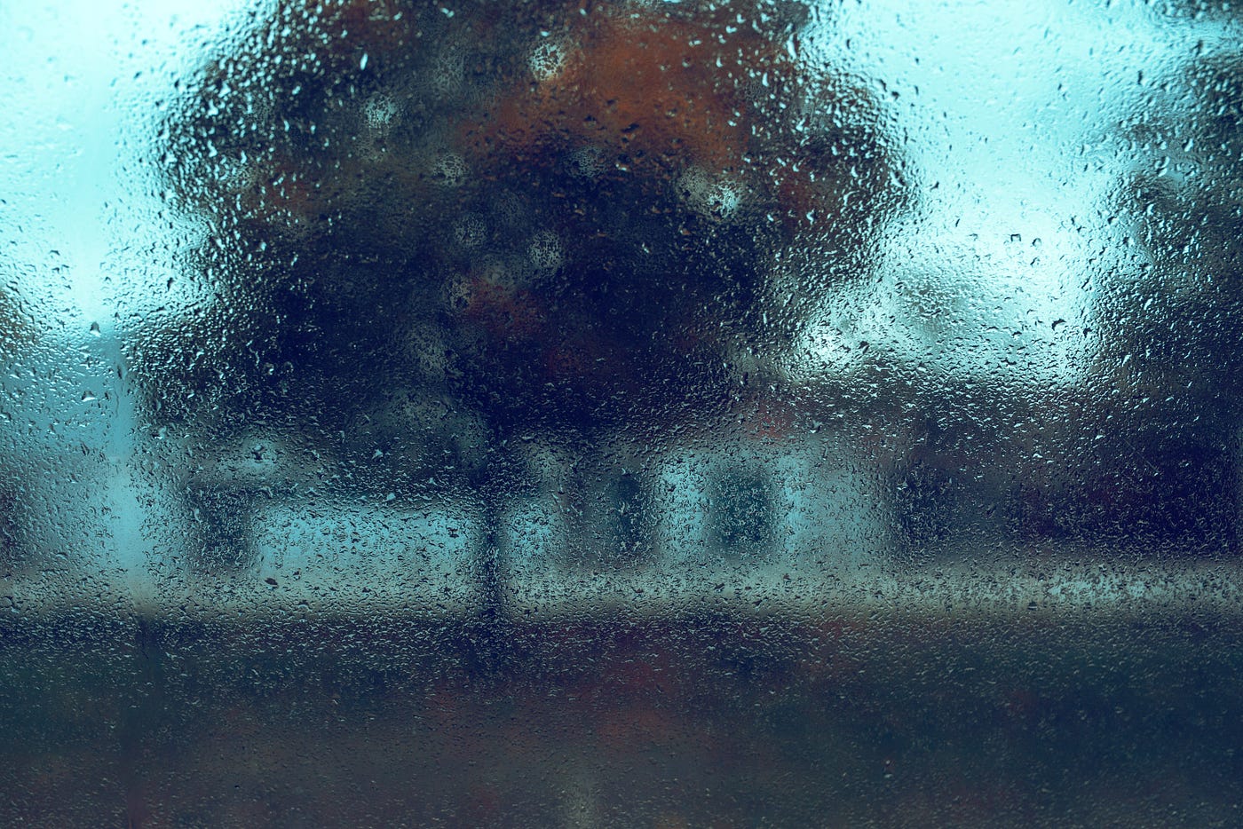 Rain on the window against a dark autumnal background of trees and houses.
