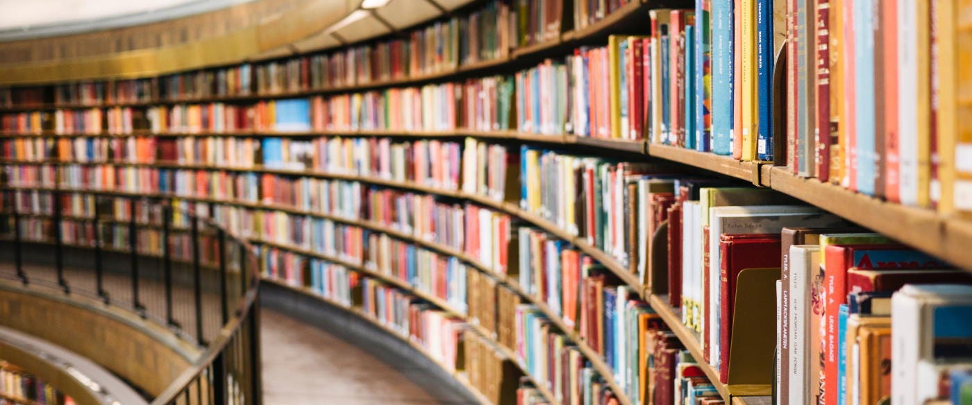Crowded bookshelves on the second floor of a library curve away into the distance