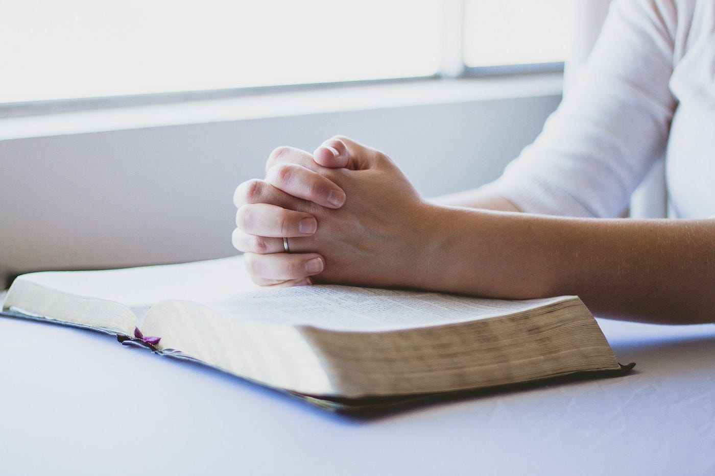 Hands clasped in prayer on top of open Bible.