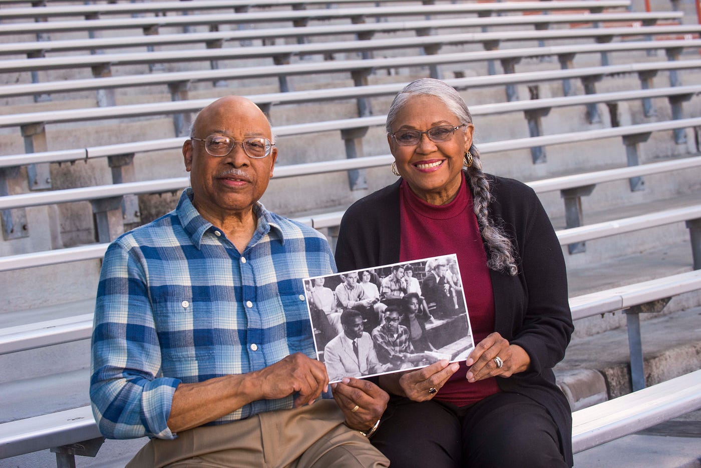 Leon and Peggy Holland sit on football bleachers in 2017 and hold a picture of themselves attending a football game as students.