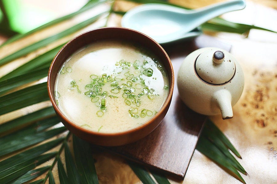 A bowl of miso sits beside a pot of tea.