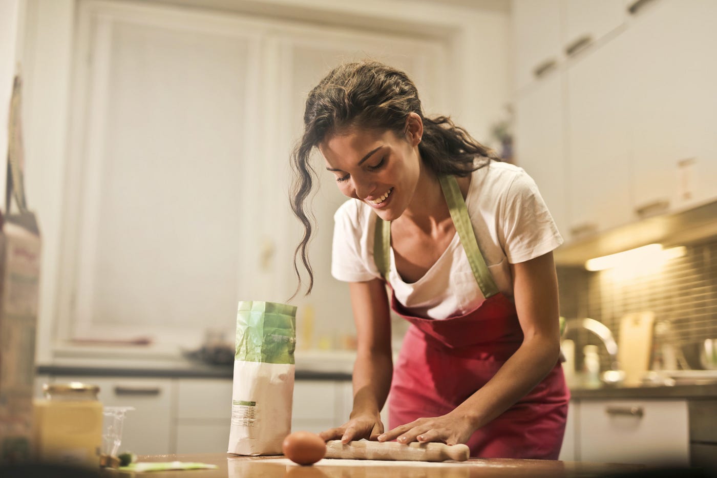 A woman in an apron uses a rolling pin on a table in the kitchen.