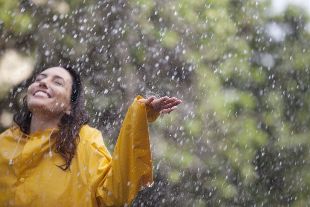 A woman in a yellow raincoat enjoying raindrops falling on her face.