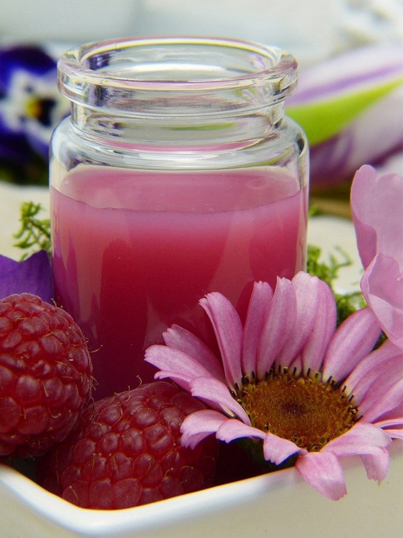 Color photo of a glass of raspberry juice, a couple of fresh raspberries and just picked, Echinacea blooms, on a table.