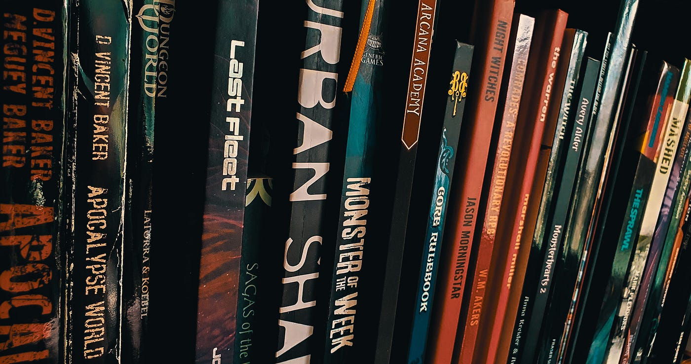 A bookshelf with many Powered by the Apocalypse games on it, starting from D. Vincent and Meguey Baker’s Apocalypse World.