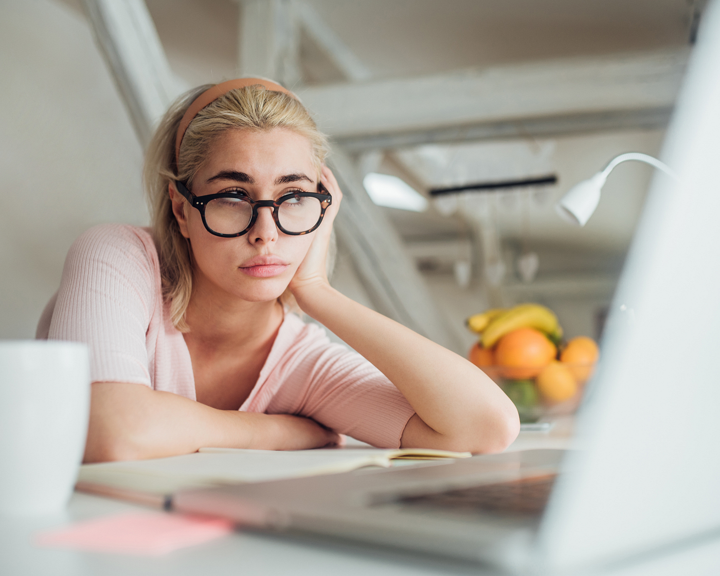 A woman wearing glasses sits in front of her laptop