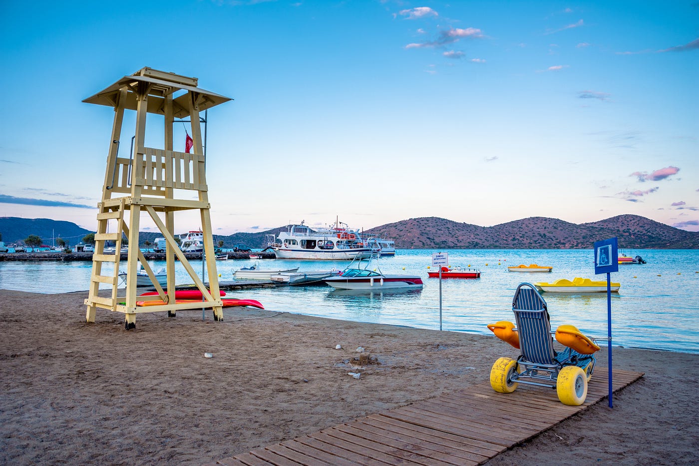 Sandy beach, with several boats, lifeguard tower and a wheelchair.