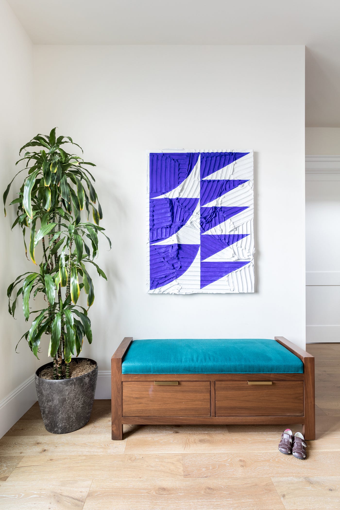 A bright foyer designed by Sarah Barnard, a blue and white abstract painting by Michelle Jane Lee and a large green house plant in a pot.