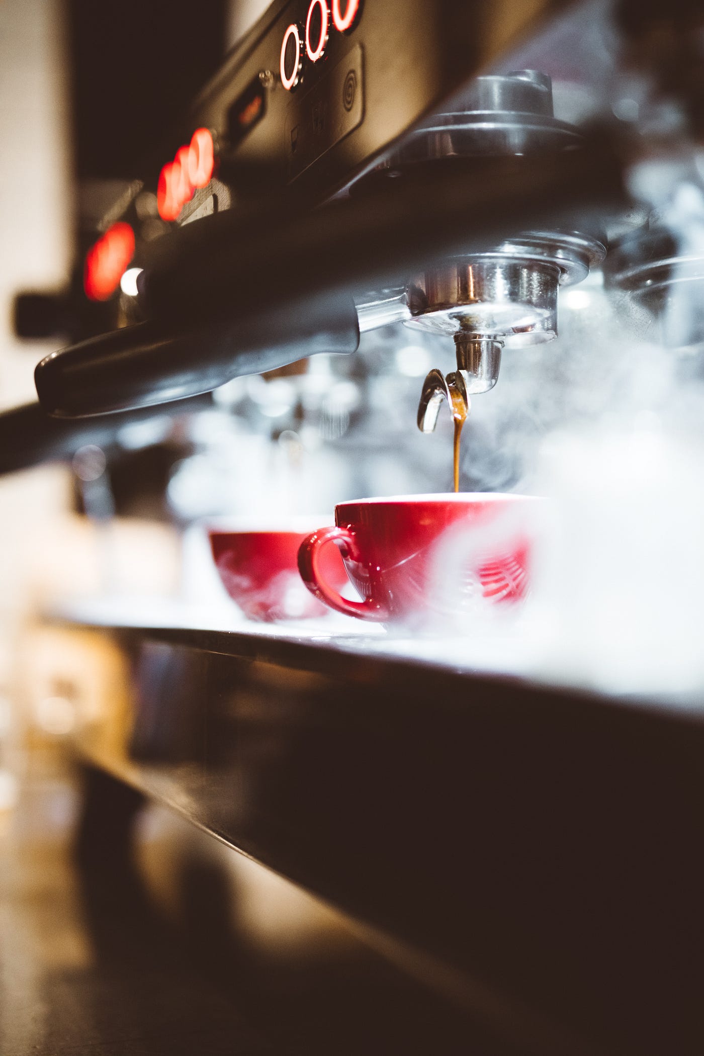 A red coffee cup centered on a coffee press with steam everywhere.
