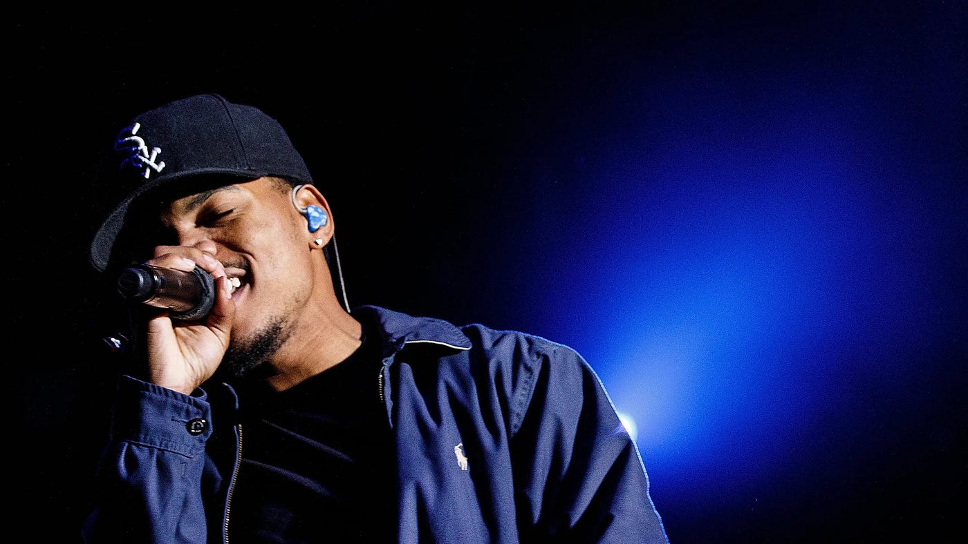 Chance the Rapper performing into mic backlit by blue light shining in the dark
