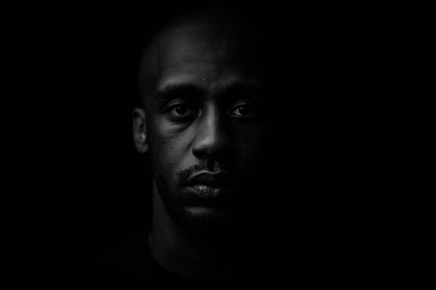 Close-up portrait of a young Black man against a black background.