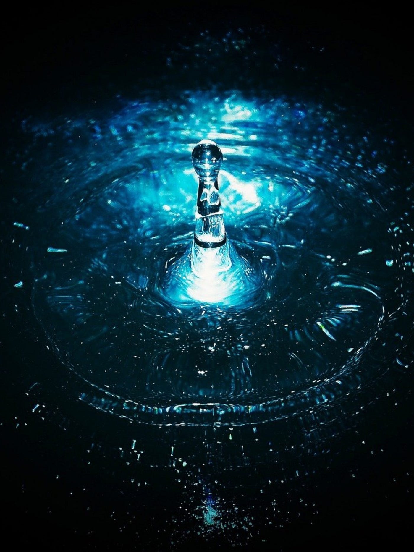 Color photo of a reverorating drop of water, giving off bluish tones of light.