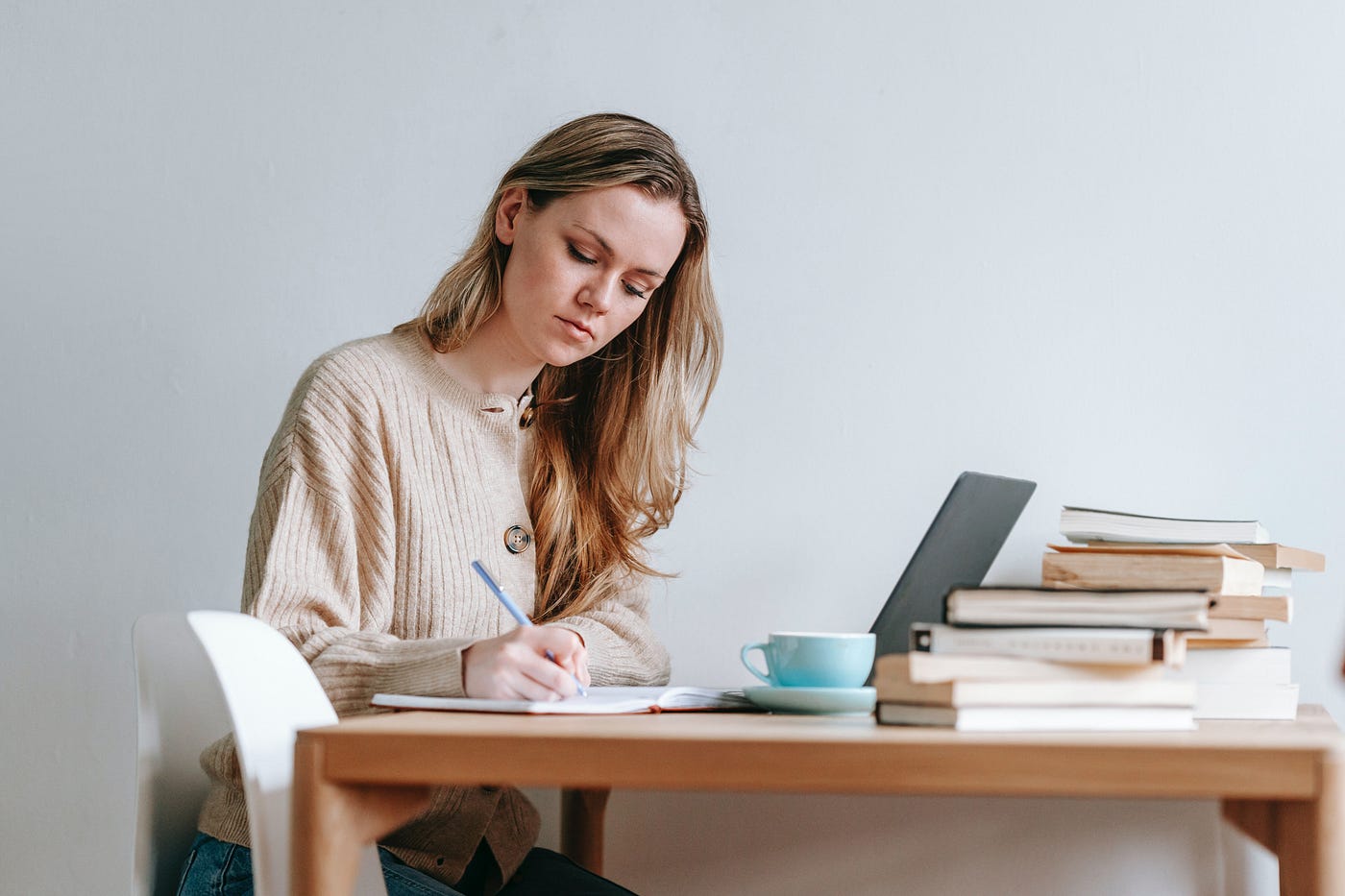 woman sitting at a desk writing in a notebook and using laptop