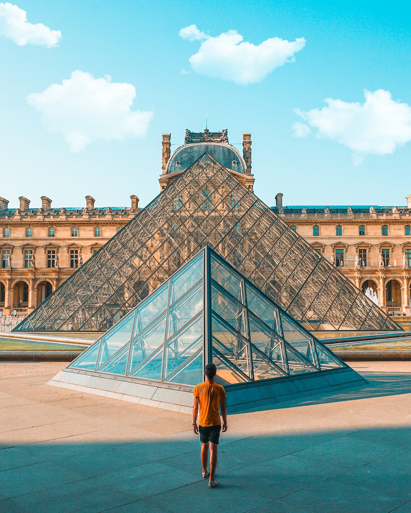 Man standing in front of two glass pyramids. These pyramids form the outside of the Louvre museum in France.