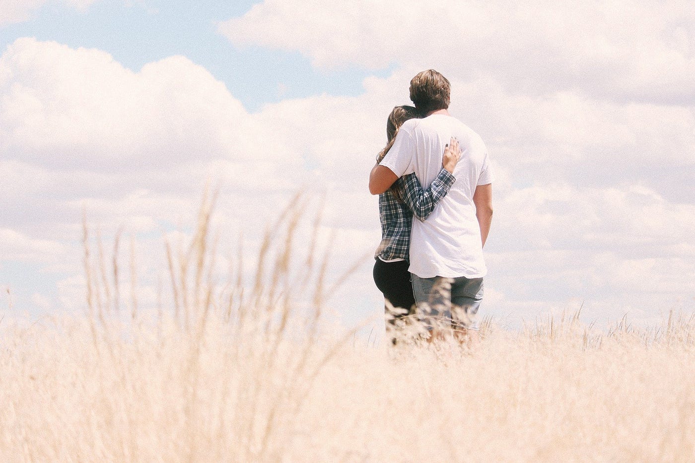 A woman and man embracing and looking over a white field under a cloudy but bright day.