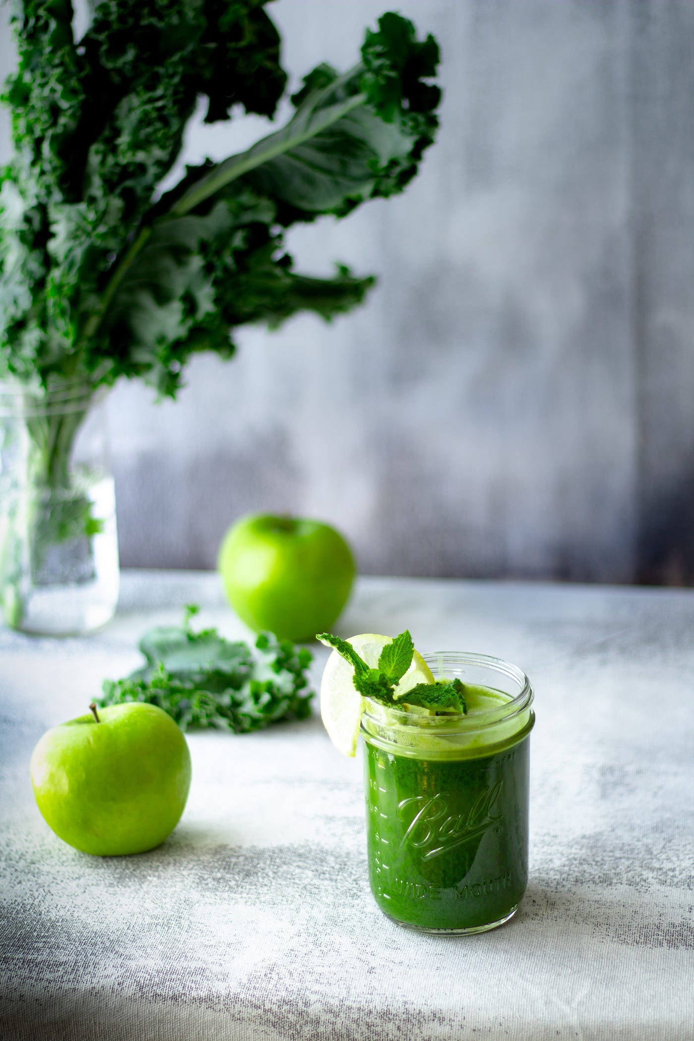 A green Juice on a counter serounded by kaile and green apples.