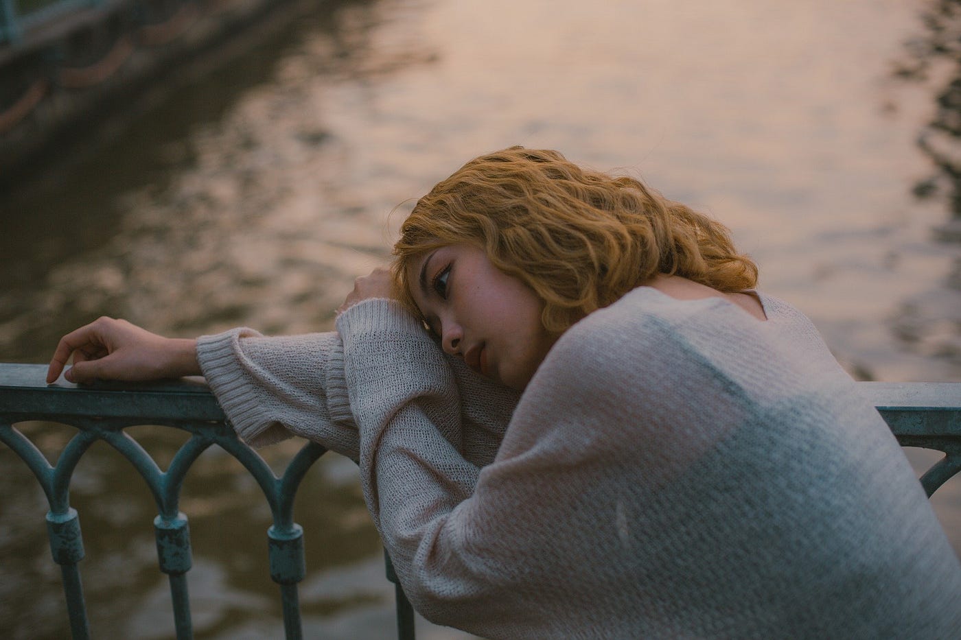 Sad young woman with head laid down on arm. Scenic water view in the background.