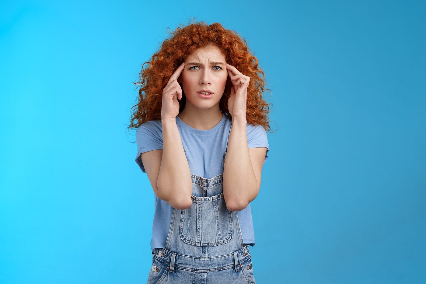 confused young woman with long red hair pressing her temples, on a blue background, Lisa Gerard Braun, Medium
