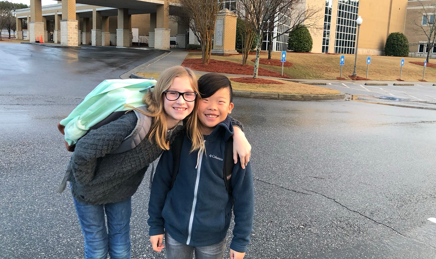Two kids smiling in front of their school