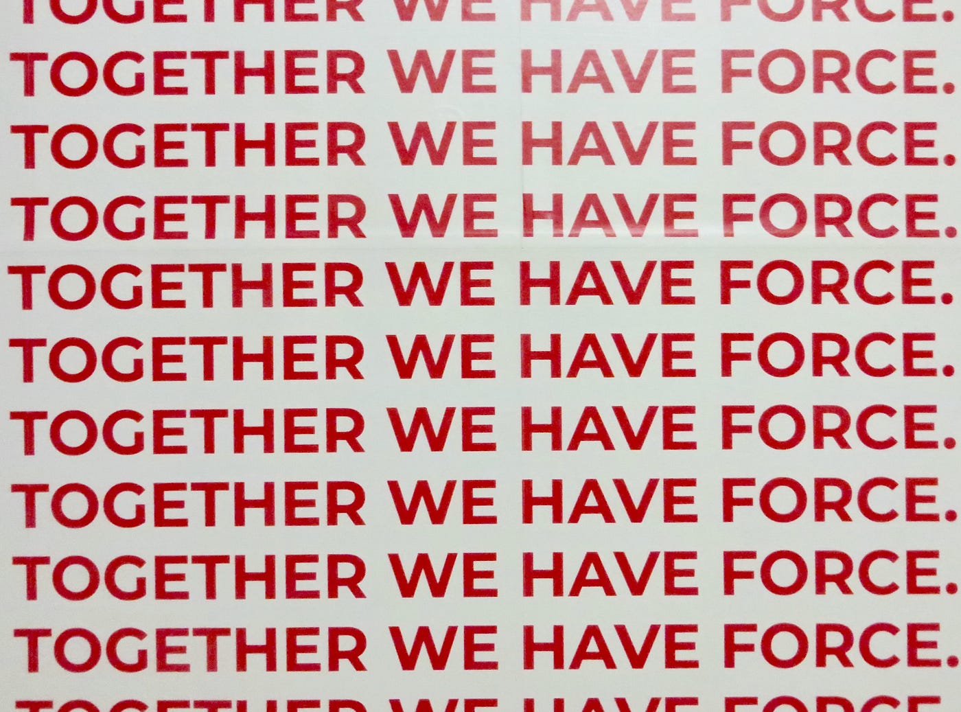 The words TOGETHER WE HAVE FORCE written atop of each other seven times inred against a geay background.
