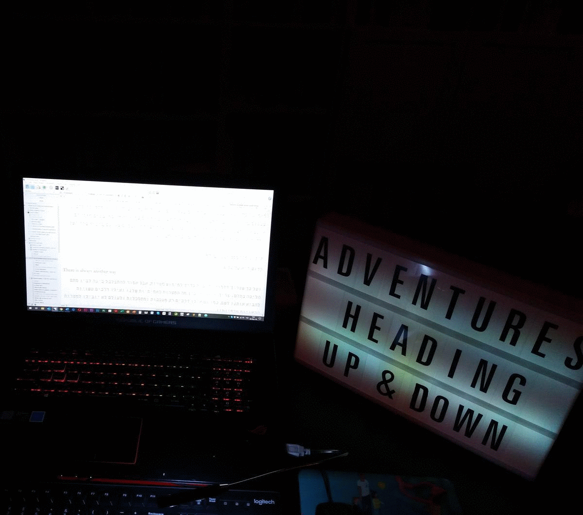 A gif of a desk with an open laptop and a lightbox with the words “ADVENTURES HEADING UP AND DOWN” over changing colors.