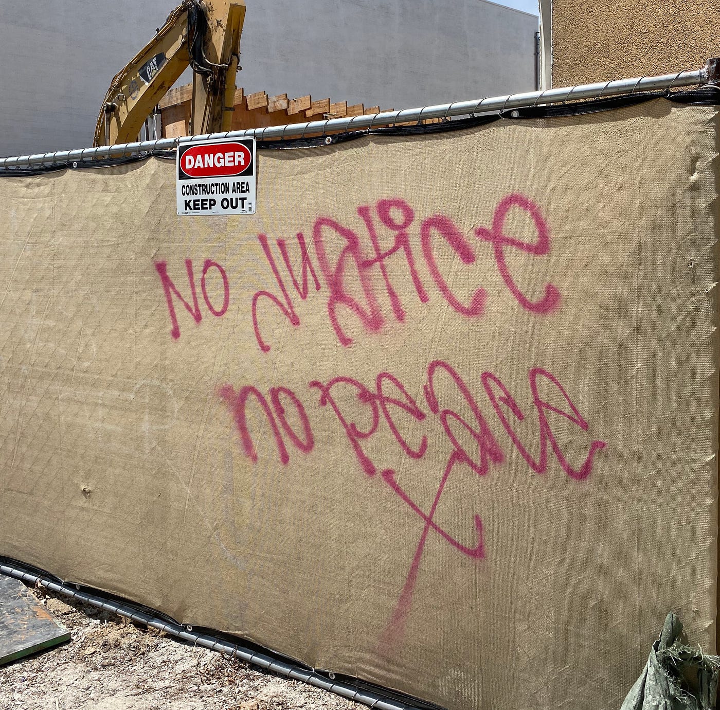 Graffiti outside of a construction site saying “No justice no peace X”