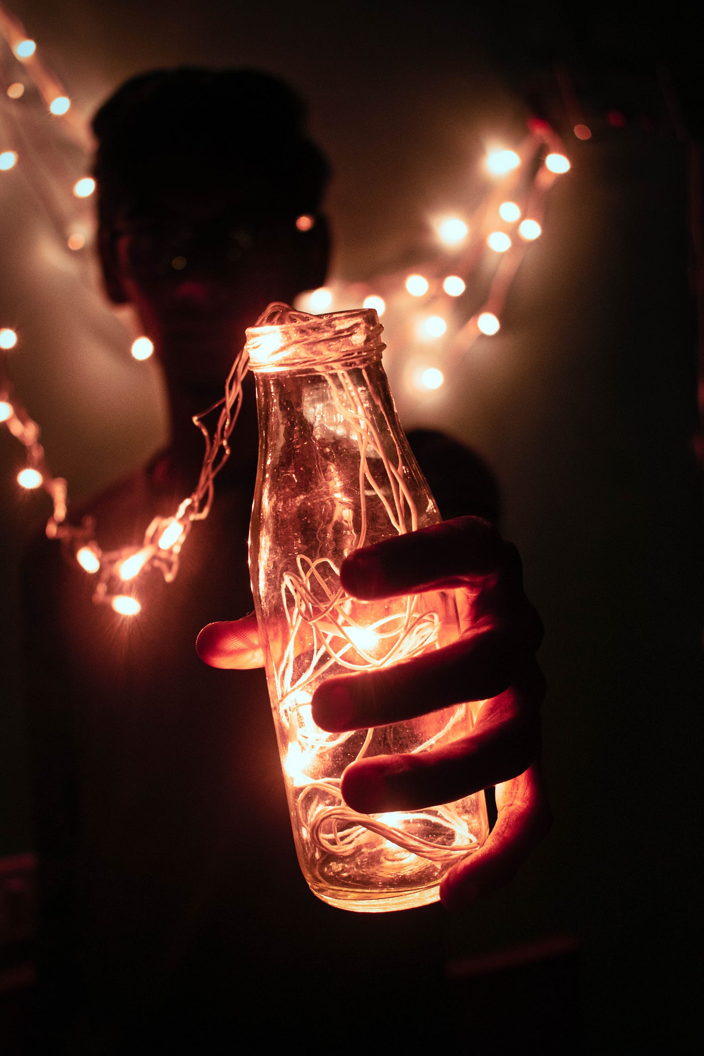 A boy holding a bottle filled with lights on a string