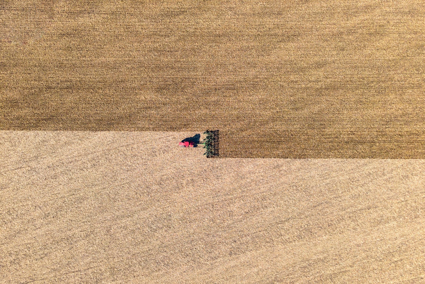 Aerial view of tractor with implement tilling a field in the country on a sunny afternoon.