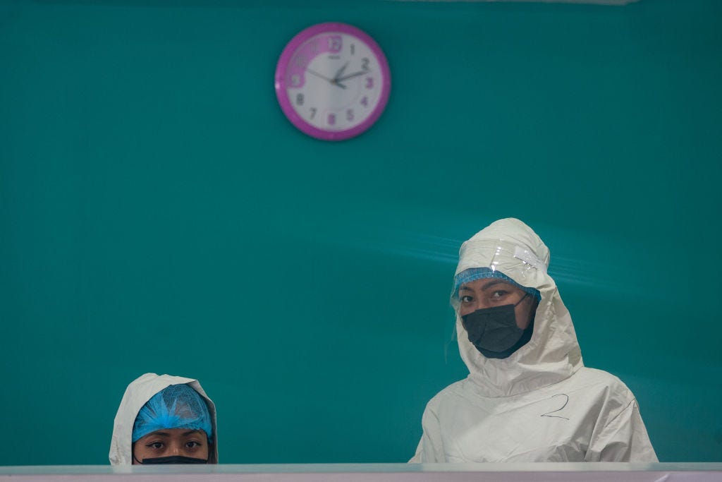 A photo of two healthcare workers wearing masks standing at a counter against a teal background.