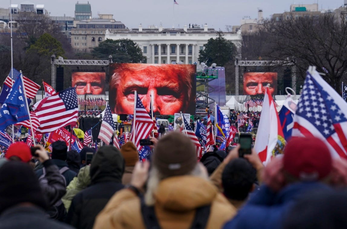Trump’s face on large screens before a crowd of people holding American flags. AP Photo/John Minchillo