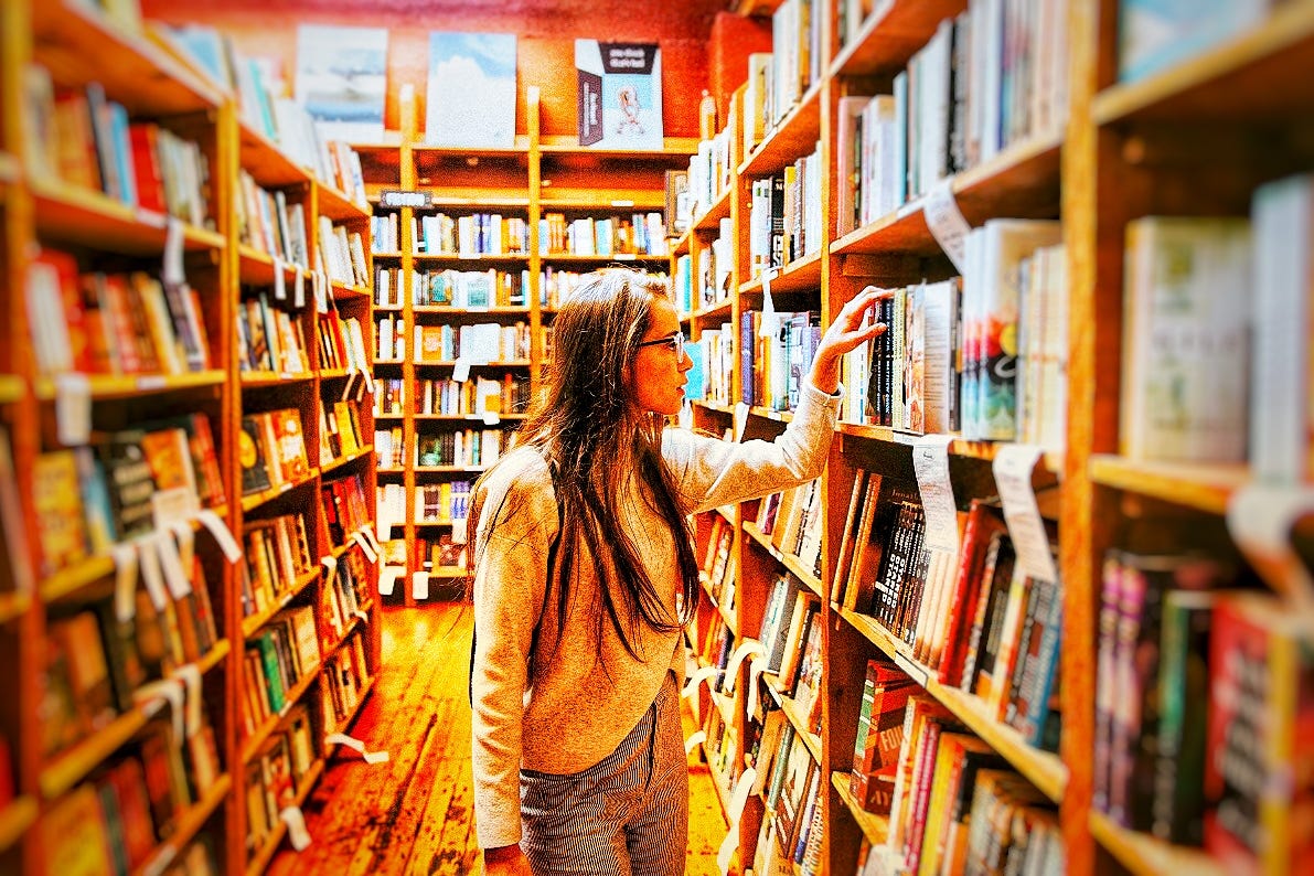 a woman in a library is reaching for a book on a shelf