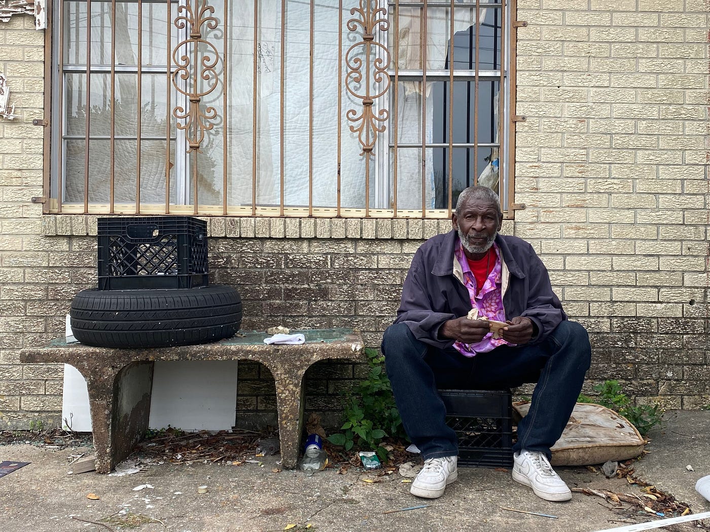 A man sitting on a milk crate on the sidewalk.