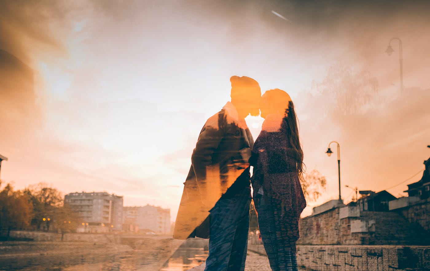Double exposure orange-filtered photo of a couple kissing against bright sky.