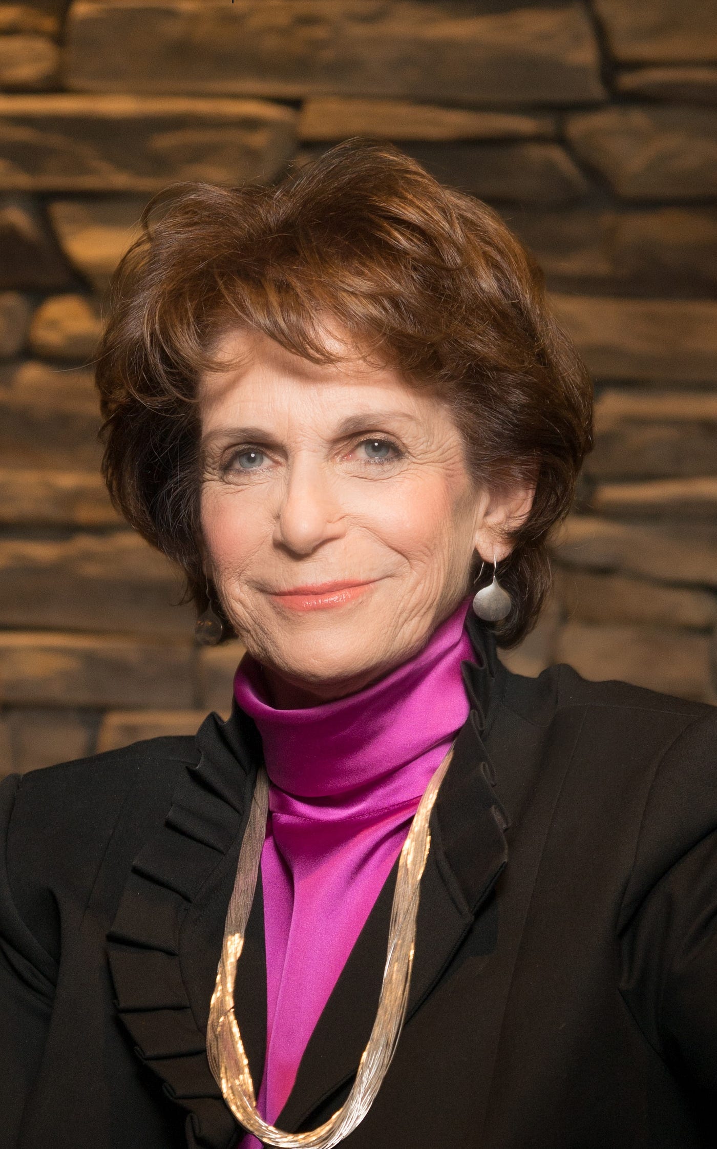 A headshot of Karen Lawrence smiling in front of a brown stone wall