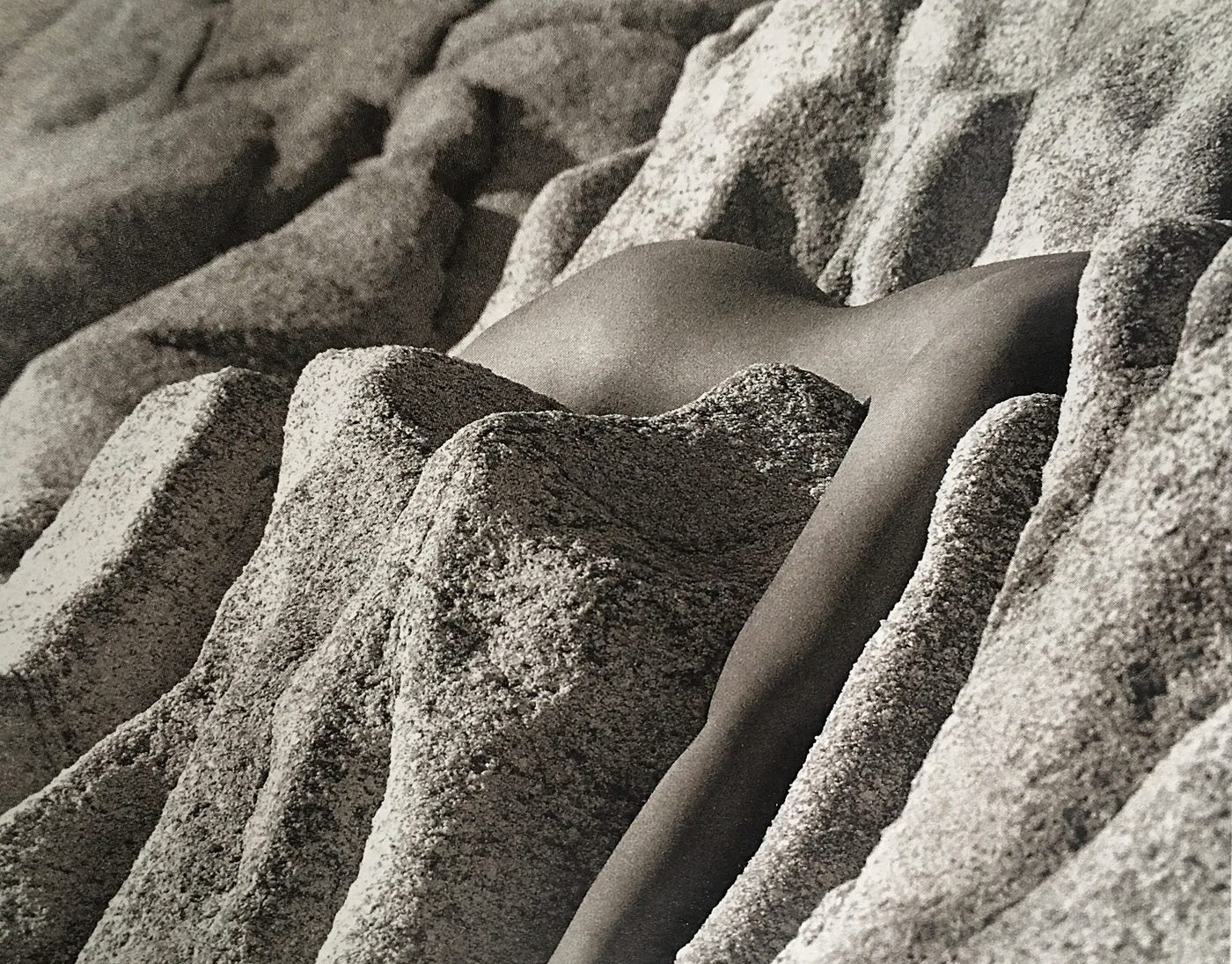 A female figure (upper buttocks, waist, lower back and one arm) rests between curious rock formations