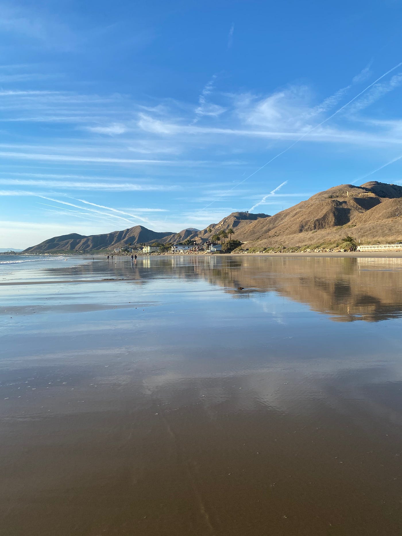 A scene at the beach with the sky reflecting itself in the water