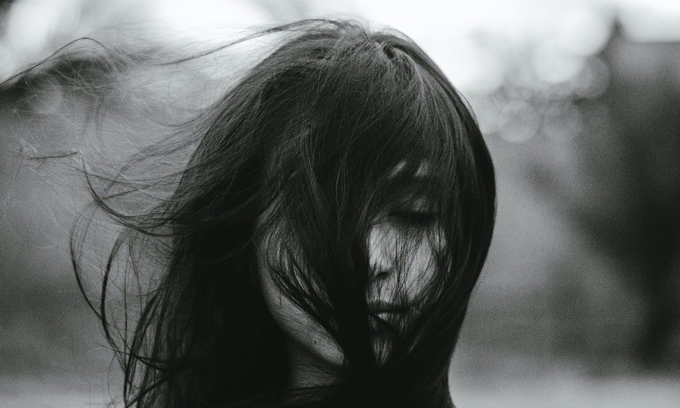 Young woman standing in wind with eyes closed.