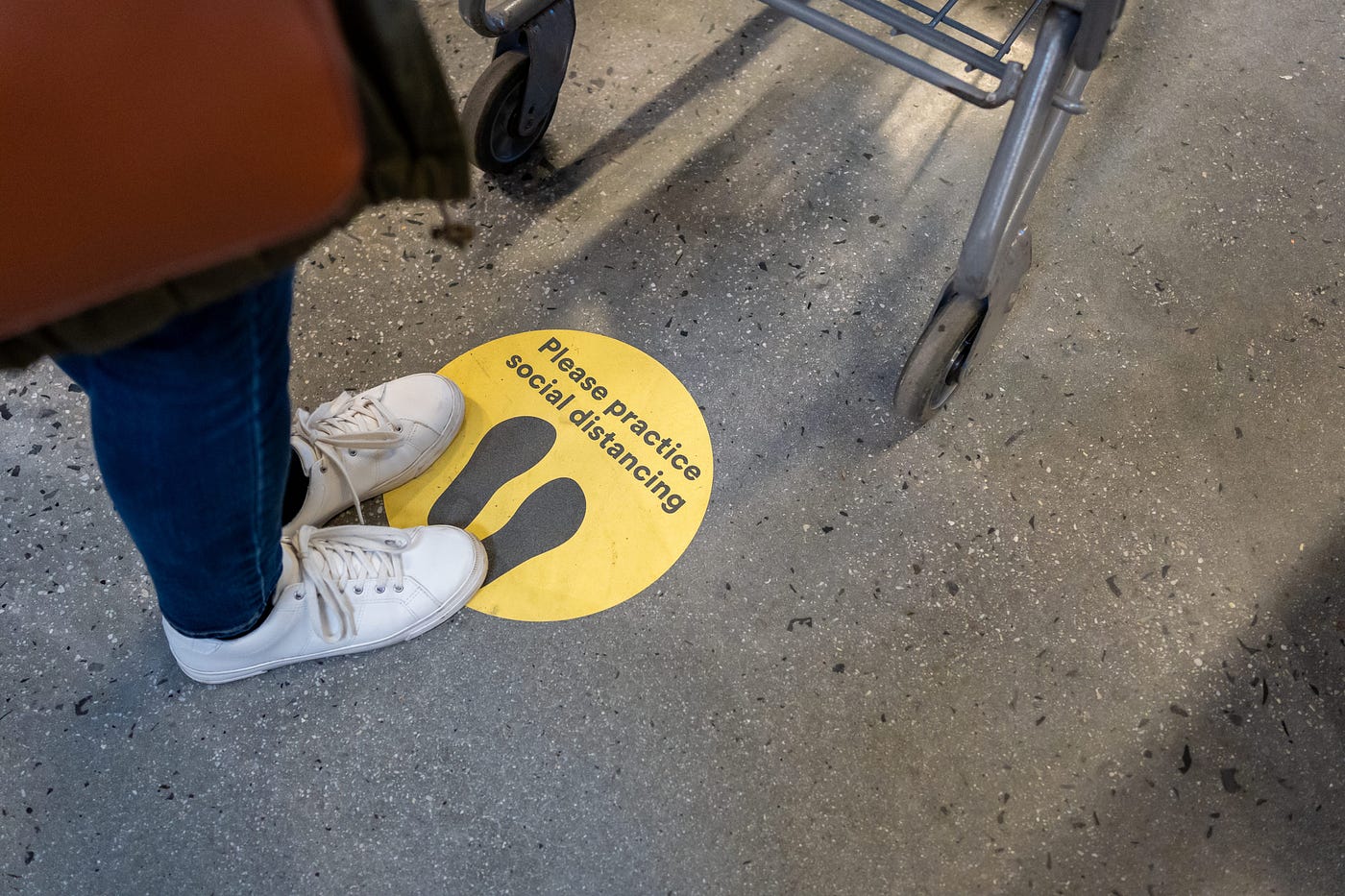 A photo of a person standing on a sticker that says “practice social distancing” at a grocery store.