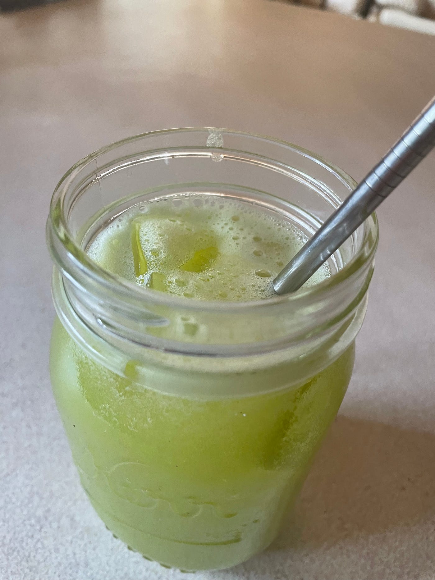 Iced celery juice in a glass jar with a straw on the counter.
