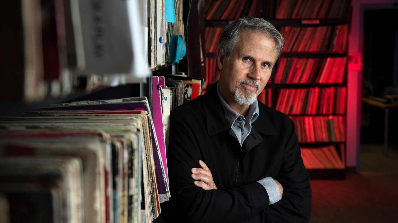 Jim Guerinot crosses his arms and leans against shelves filled with records