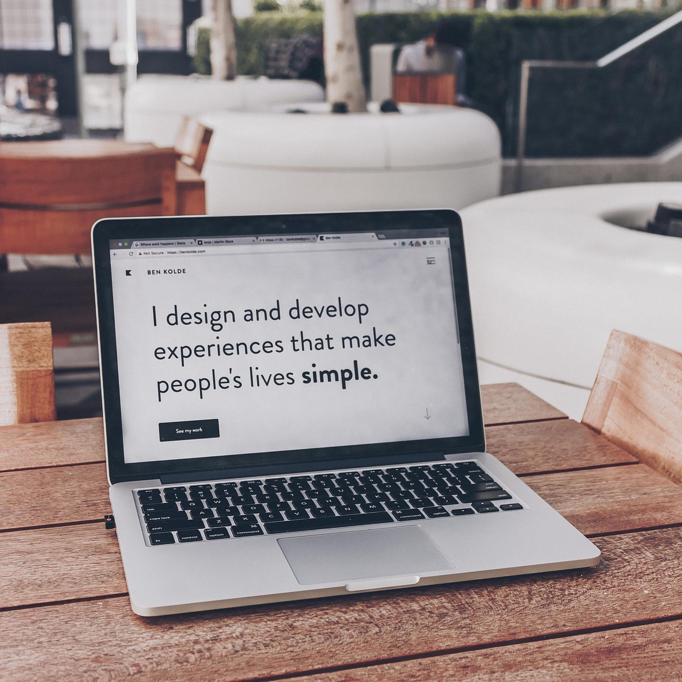 A notebook is positioned on top of a wooden table with an open website. On this site, there is an text that says: “I design and develop experiences that make people’s lives simple”