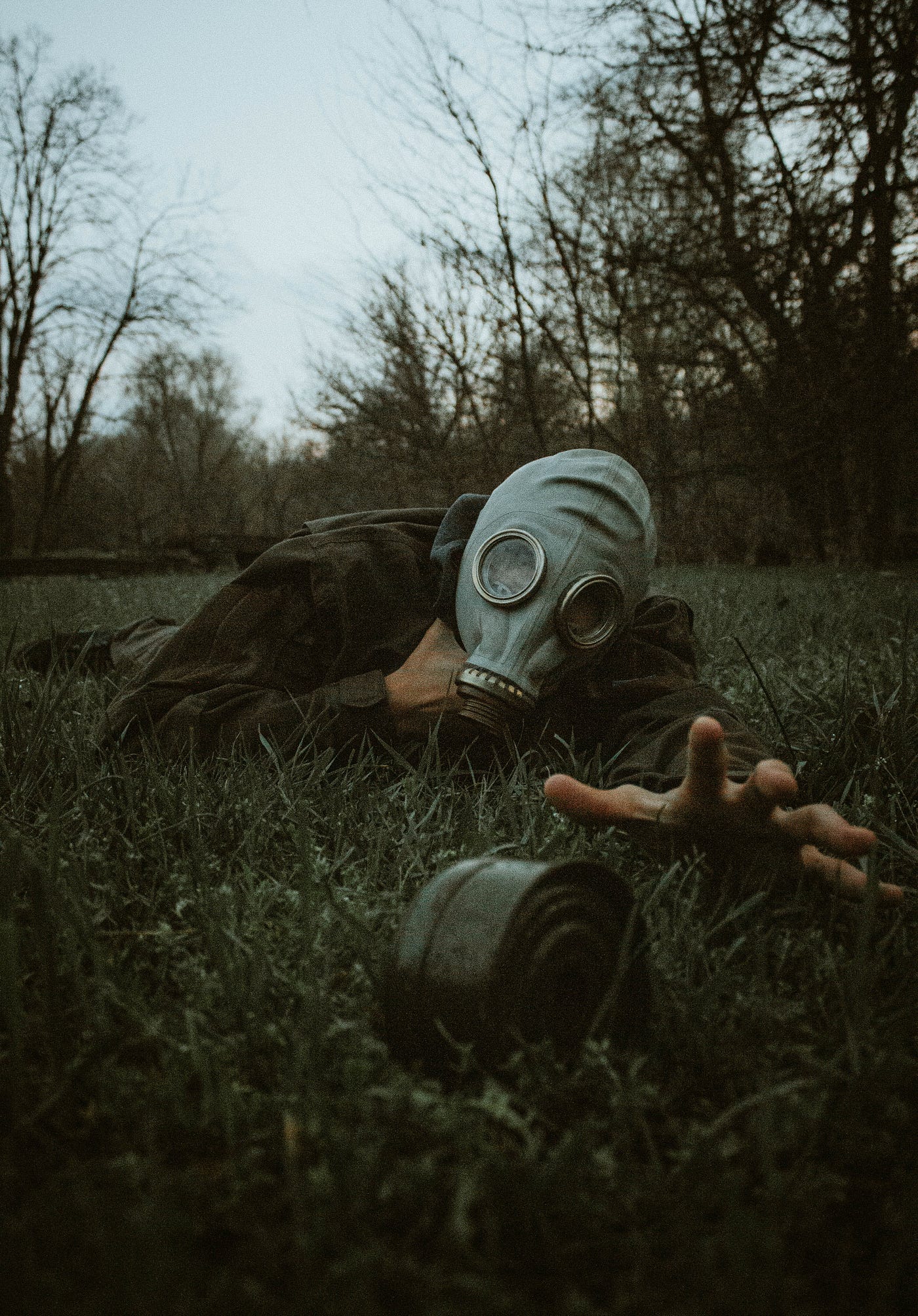 person wearing a gasmask crawling in a field reaching for a mine. perspective- towards you.